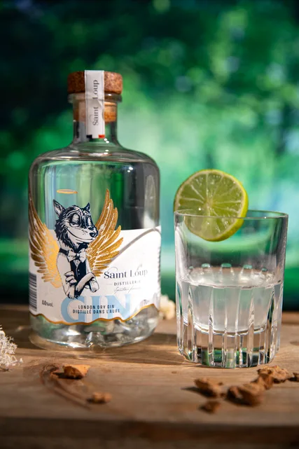 Une bouteille de gin artisanal et son verre au citron vert, sur une table en bois.