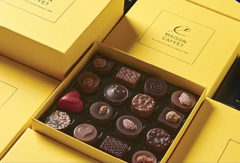 Un coffret jaune Maison Caffet ouvert sur un assortiment de chocolats.