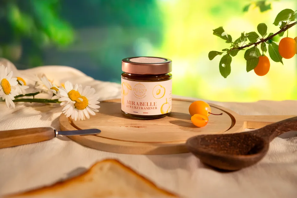 Un pot de confiture d'abricot sur une table fleurie, cuillère en bois et tartine à côté.
