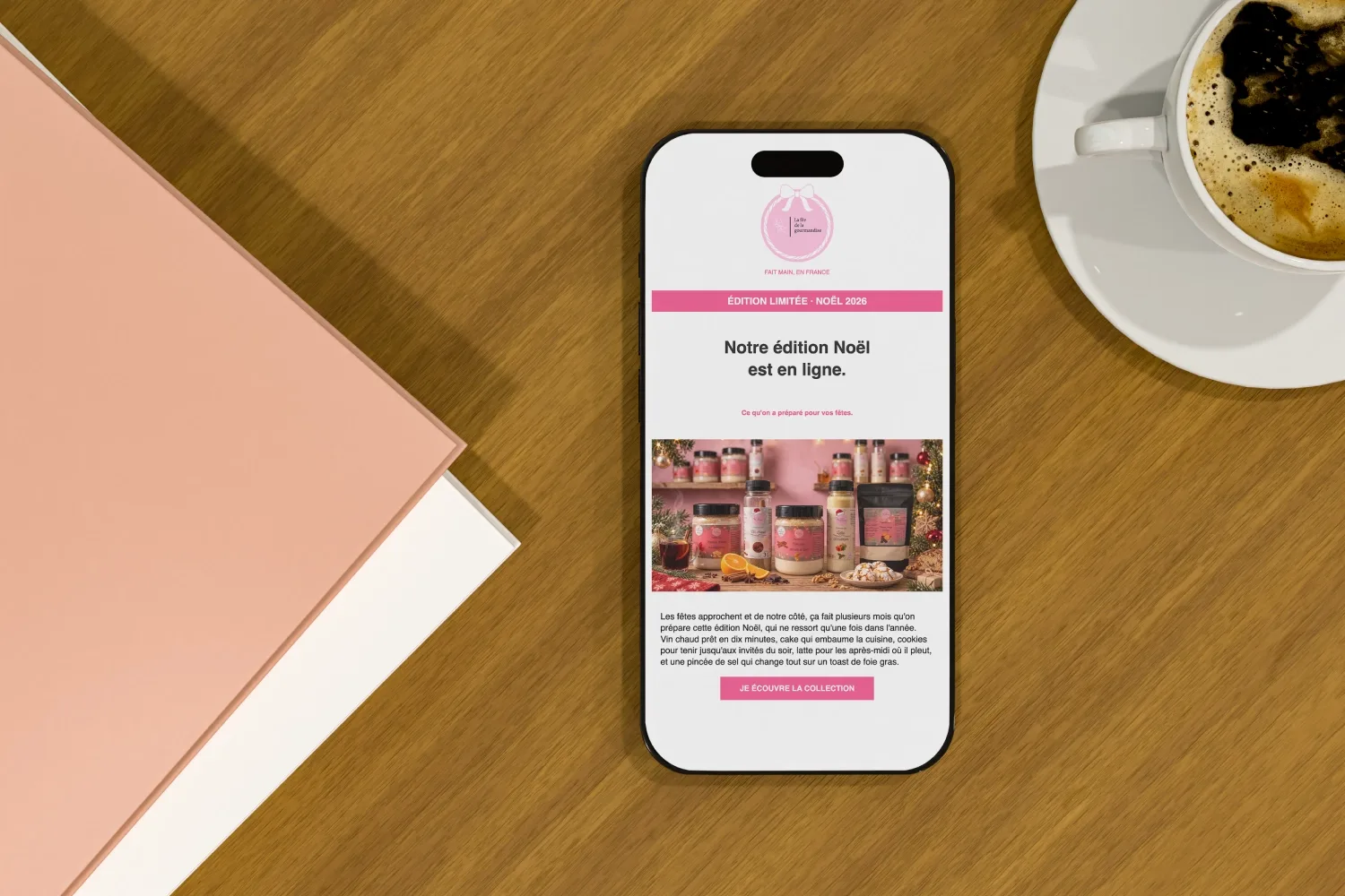 L'emailing « Notre édition Noël est en ligne » de La Fée de la Gourmandise affiché sur un téléphone posé sur une table en bois.