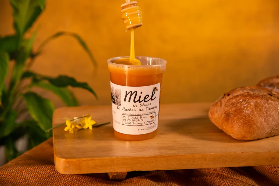 Un pot de miel et sa cuillère à miel, à côté d'un pain de campagne.
