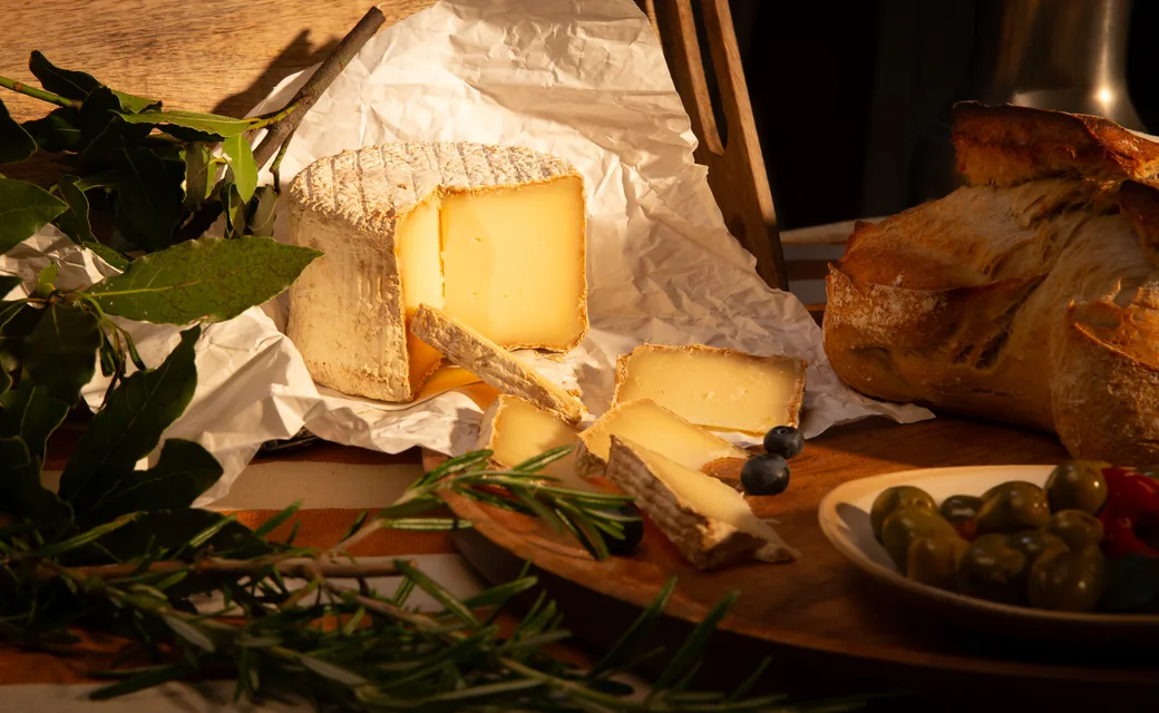 Une tranche de fromage et des herbes fraîches sur la table, en lumière chaude.