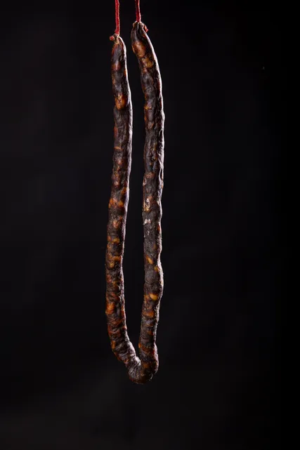 Un saucisson fin suspendu, sur fond noir.