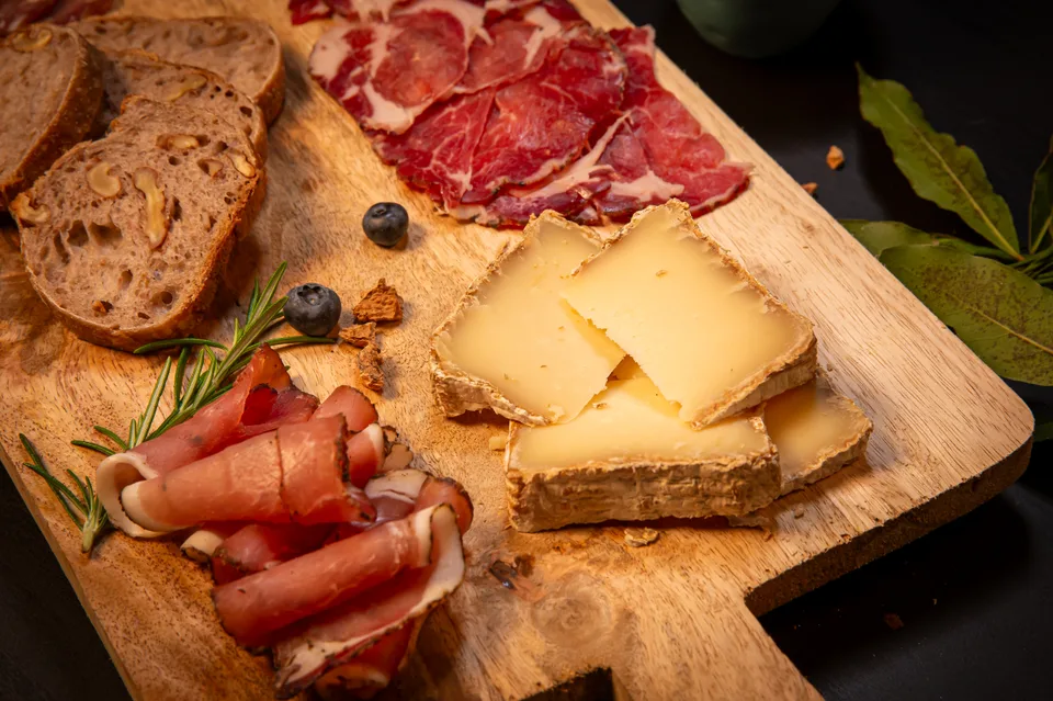 Charcuteries et fromage tranchés sur une planche en bois, avec du pain.
