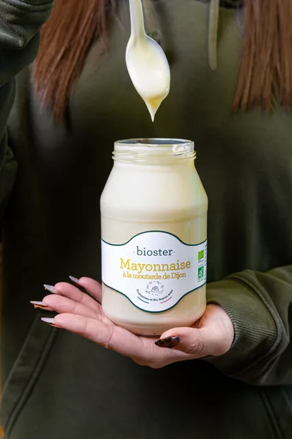 Un pot de mayonnaise Bioster et sa cuillère, tenu en main.