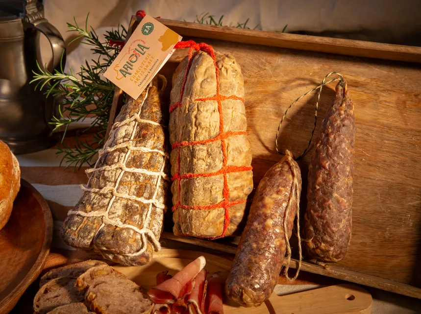 Des charcuteries ficelées présentées dans une caisse en bois avec du romarin.