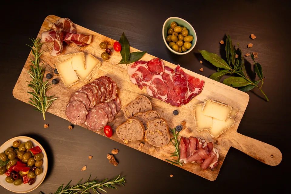 Une planche de charcuteries et de fromages, avec olives et tomates cerises.