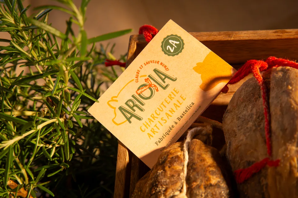 Une charcuterie Ariola et son étiquette, posée parmi le romarin et le pain.