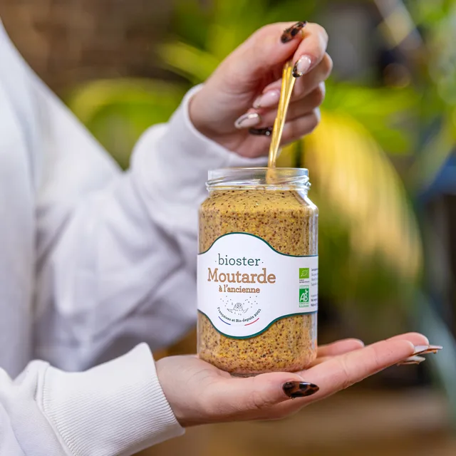 Une cuillère plongée dans un pot de moutarde Bioster.