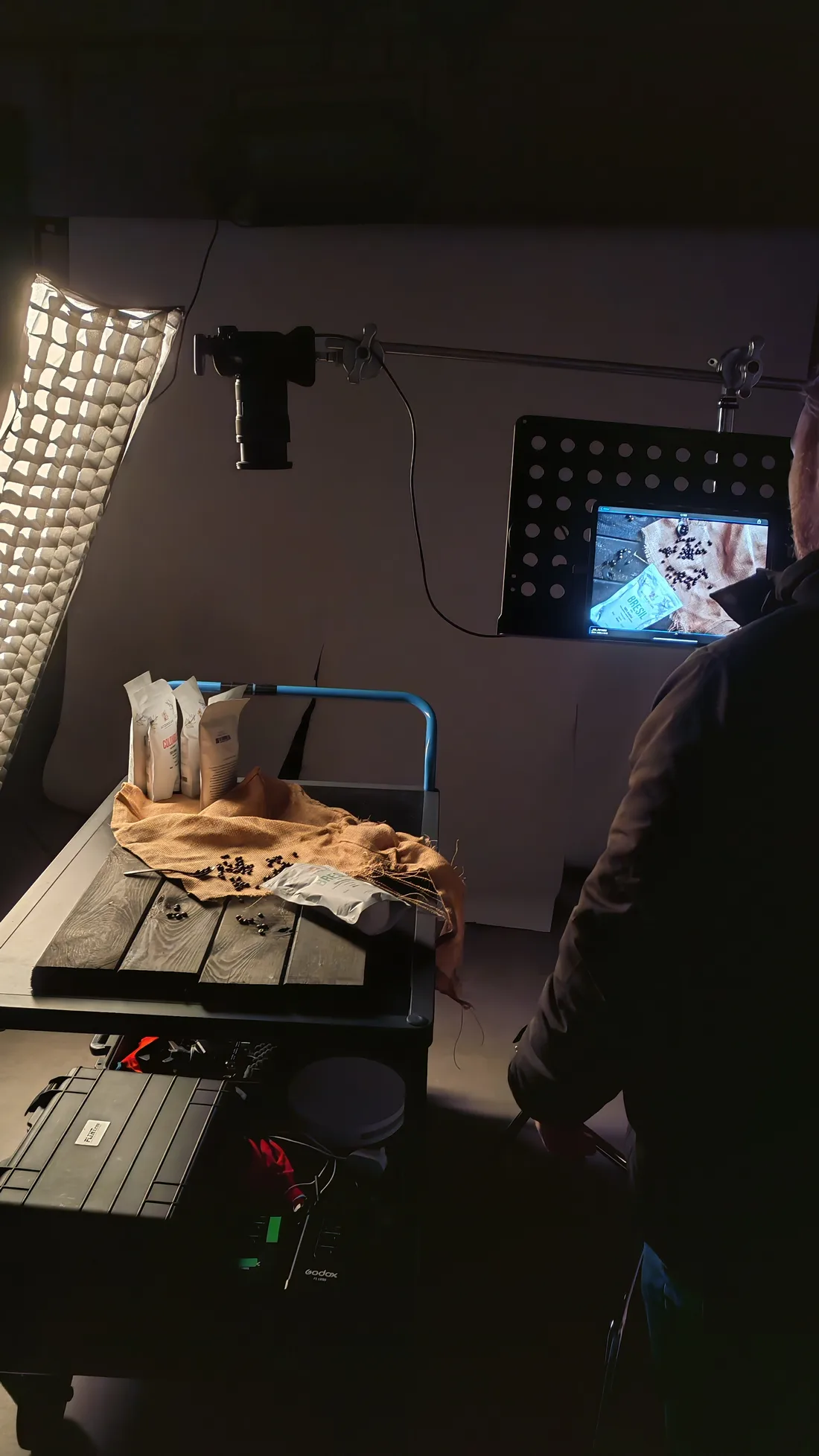 Un shooting produit au studio : sachets et grains posés sur une table, éclairage en lumière rasante, l'image contrôlée en direct sur écran.
