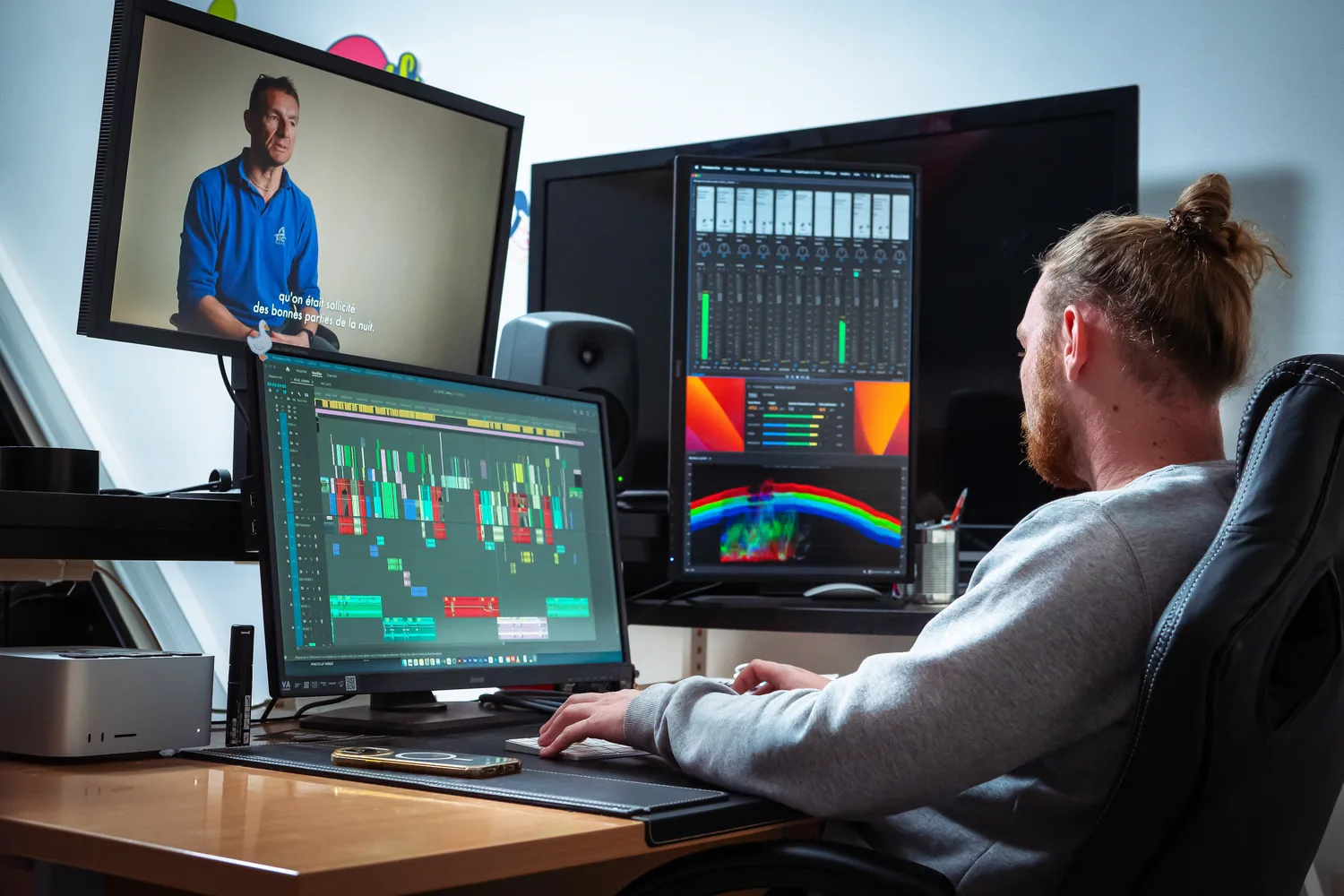 Un monteur de l'agence à son poste de post-production : montage, vumètres et console de mixage à l'écran.