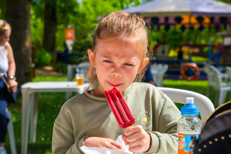 Une petite fille savoure une glace à l'eau rouge en terrasse, au parc Grinyland.
