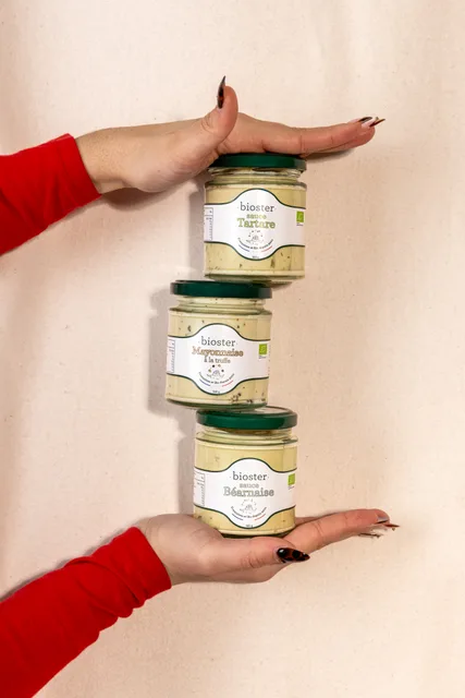 Trois pots Bioster empilés entre deux mains, sur fond clair.